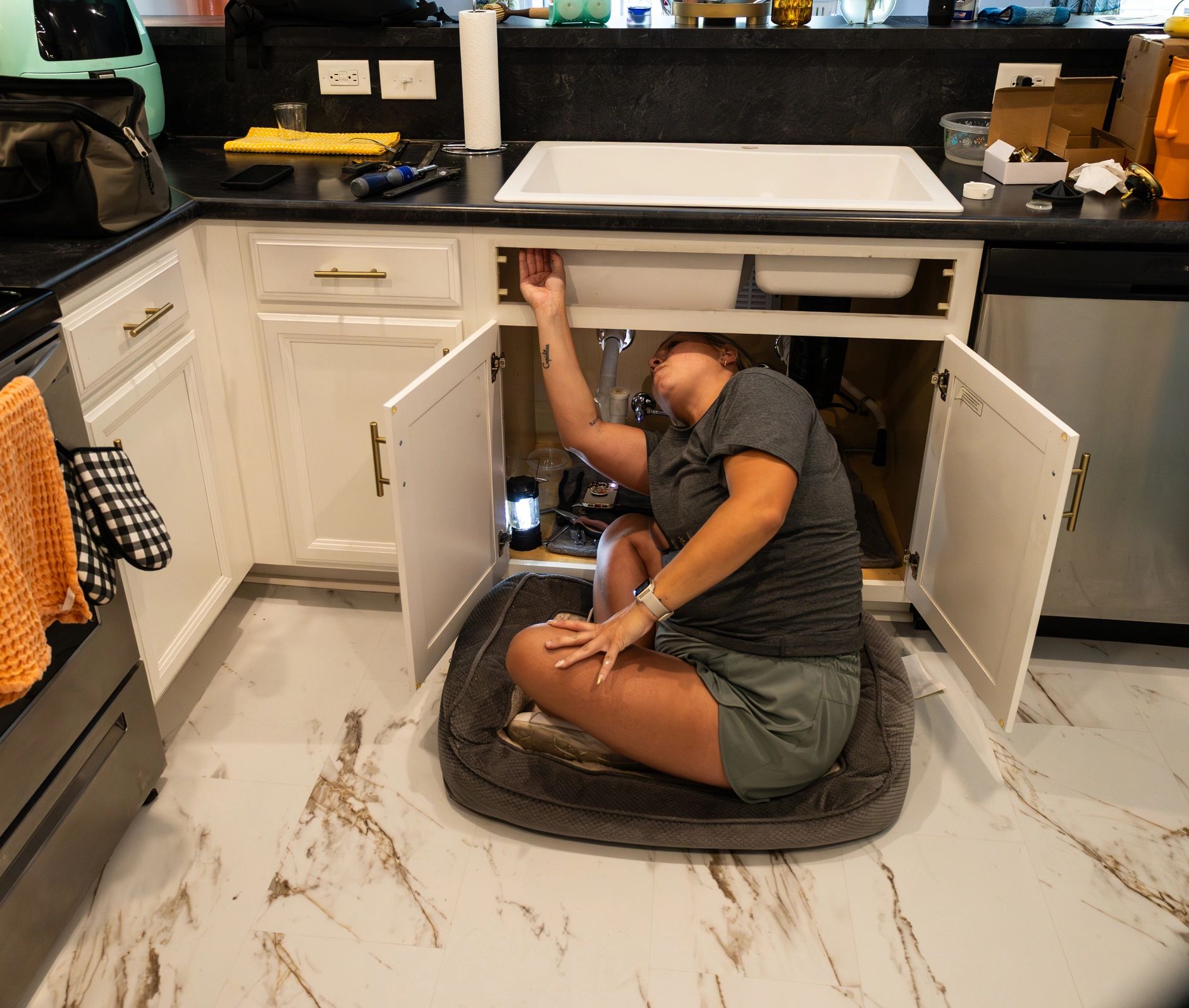 Plumber carrying out plumbing repair beneath a kitchen sink